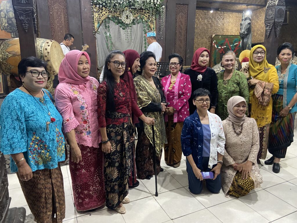 Group of women in colorful traditional outfits posing indoors at a cultural venue.