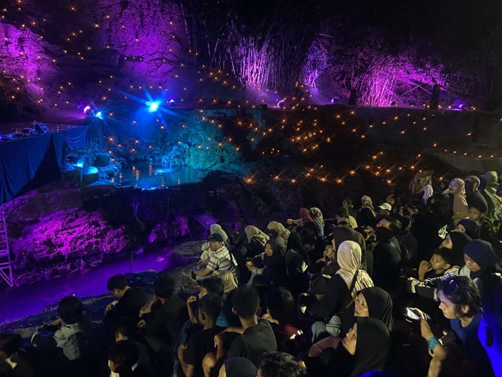 IMG_5049 - Mabur.co Audience seated on stone steps in a dark cavern lit by purple and blue lights with string fairy lights overhead.