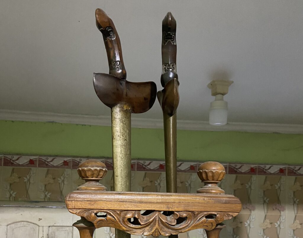 Antique wooden fireplace tool set on an ornate stand with tall tongs and brass columns in a vintage room.