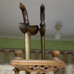 Antique wooden fireplace tool set on an ornate stand with tall tongs and brass columns in a vintage room.