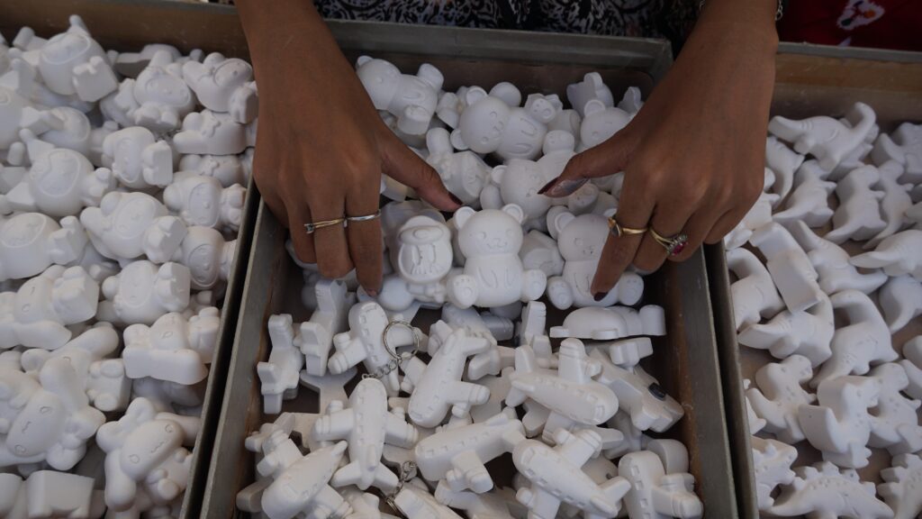 Hands with rings sorting small white bear-shaped figurines in a wooden crate filled with toys.