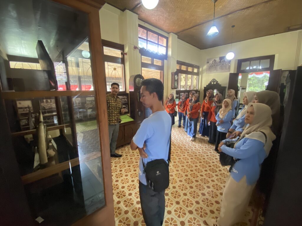 Group of students in blue uniforms listening to a guide inside a museum gallery with glass display cases.