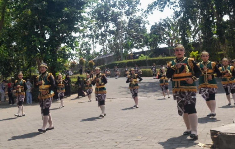 Group of dancers in green and gold traditional costumes performing a parade on a sunny day in a park or square.