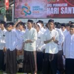 Group of people in white traditional outfits standing in a parade, with a colorful Hari Santri banner in the background.