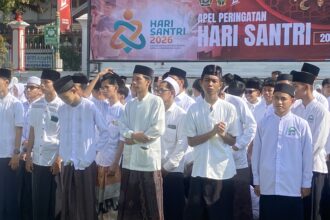 Group of people in white traditional outfits standing in a parade, with a colorful Hari Santri banner in the background.