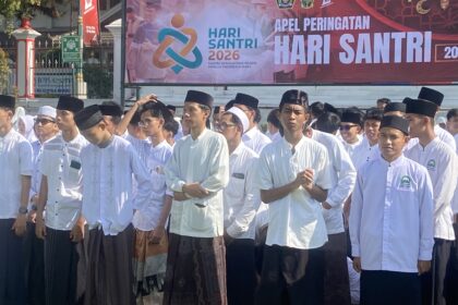 Group of people in white traditional outfits standing in a parade, with a colorful Hari Santri banner in the background.
