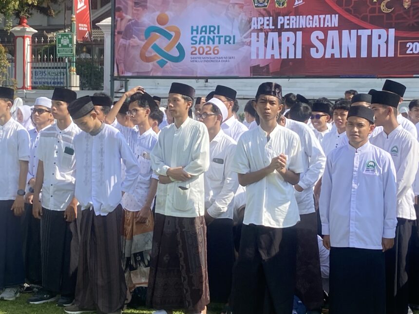 Group of people in white traditional outfits standing in a parade, with a colorful Hari Santri banner in the background.