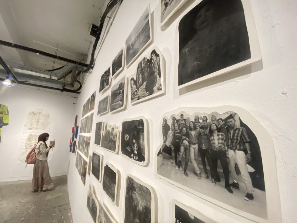 Visitor with a backpack stands in a white-washed gallery, viewing a wall covered with black-and-white photos in various sizes and frames.