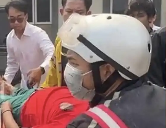Rescue workers in a white helmet and mask attend to a person covered in red on a stretcher, as bystanders look on.