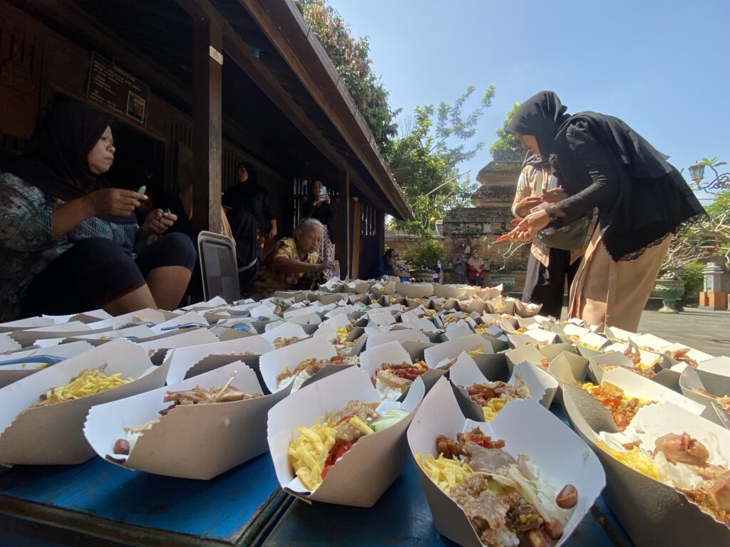 Row of takeout boxes filled with rice and toppings lined up on a blue table at an outdoor gathering with people nearby.