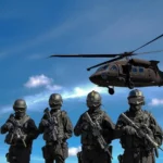Four soldiers in black tactical gear and rifles stand in formation with a helicopter hovering in the blue sky behind them, suggesting a military operation.