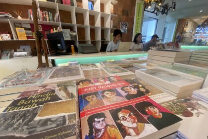 Bookstore checkout area with three people at laptops behind a display of colorful magazines to the foreground shows glossy covers; shelves in back.