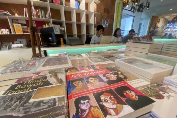 Bookstore checkout area with three people at laptops behind a display of colorful magazines to the foreground shows glossy covers; shelves in back.