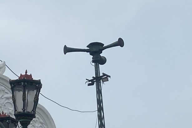Ornate street lanterns mounted on a white building, with a tall antenna/siren apparatus on top of the structure behind them.