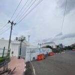 Street scene with construction barriers and white decorative gate on a cloudy day, power lines overhead
