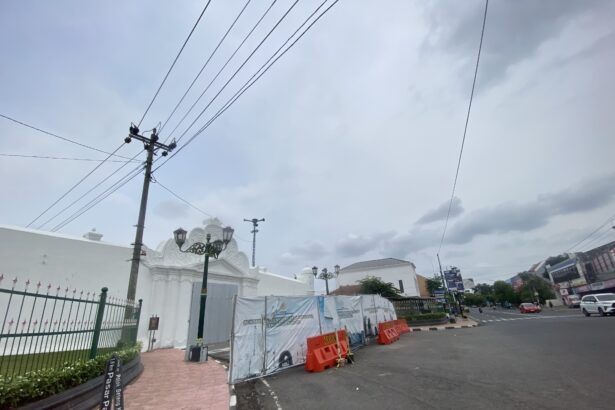Street scene with construction barriers and white decorative gate on a cloudy day, power lines overhead