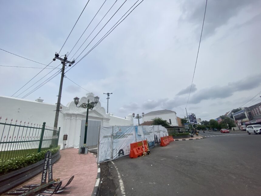 Street scene with construction barriers and white decorative gate on a cloudy day, power lines overhead