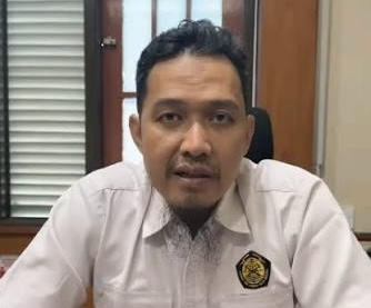 IMG_6375 - Mabur.co Man in a white shirt with a badge sits at a desk in an office, facing the camera.