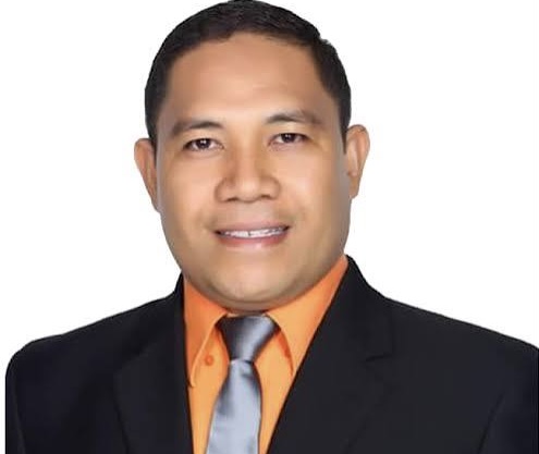 Professional headshot: man in a black suit, orange shirt, and gray tie against a white background.