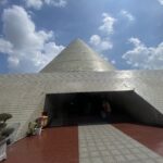 Cone-shaped silver dome atop a tiled, low-slung building with an open entrance and blue sky