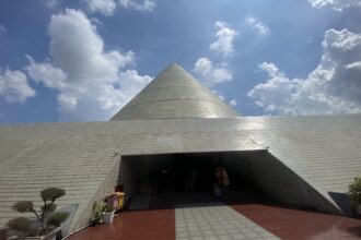 Cone-shaped silver dome atop a tiled, low-slung building with an open entrance and blue sky