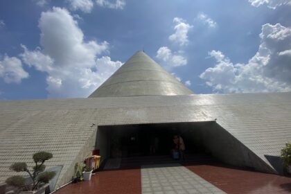 Cone-shaped silver dome atop a tiled, low-slung building with an open entrance and blue sky