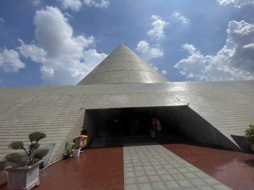 Cone-shaped silver dome atop a tiled, low-slung building with an open entrance and blue sky
