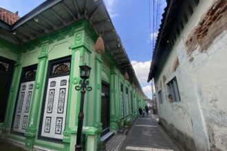 Bright green building with ornate white doors along a narrow alley; wicker lamps hang from the roof and blue sky above.