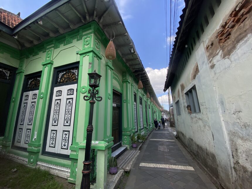 IMG_7361 - Mabur.co Bright green building with ornate white doors along a narrow alley; wicker lamps hang from the roof and blue sky above.