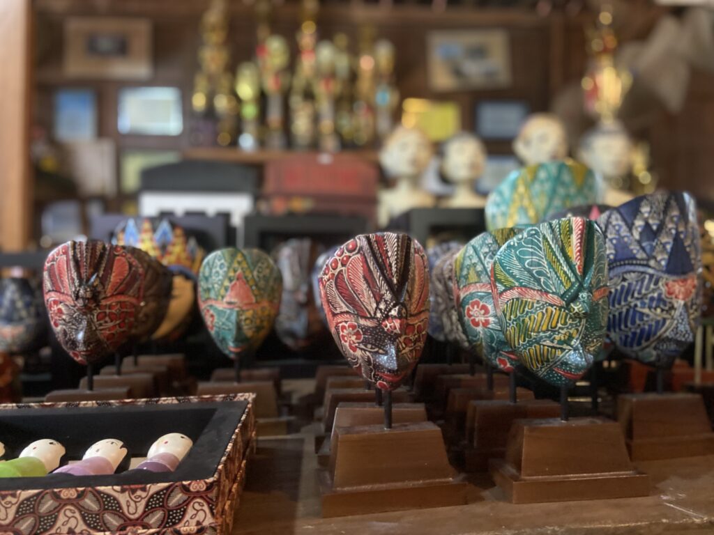 IMG_7408 - Mabur.co Row of colorful fabric-wrapped hat sculptures on display in a craft shop with blurred shelves in the background.