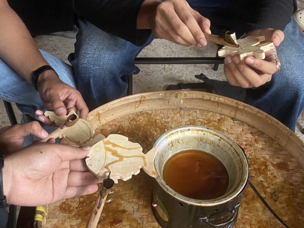 IMG_7412 - Mabur.co Hands carving a wooden piece, with curling wood shavings scattered on a round wooden surface