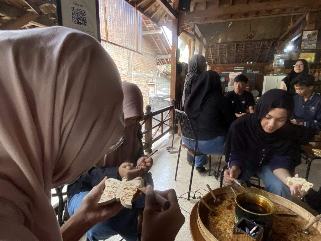IMG_7421 - Mabur.co Group of people in hijabs seated around a rustic cafe-style table, crafting wooden blocks with drawings amid a wooden interior.