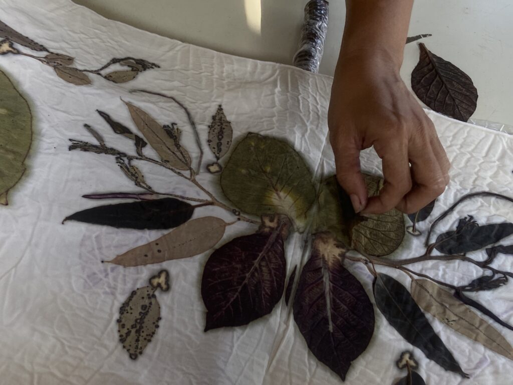 Close-up of a hand arranging dried leaves on a botanical leaf-patterned quilt or fabric.