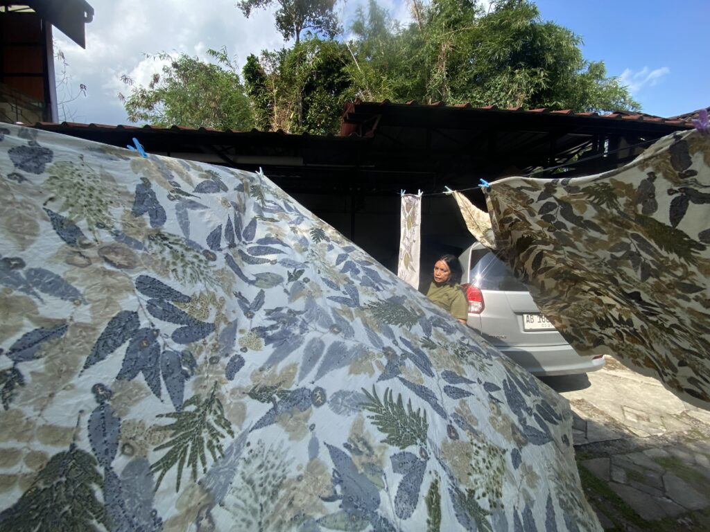 Clothesline with large camouflage-pattern fabrics drying; a woman in green stands near a silver car in daylight outdoors.