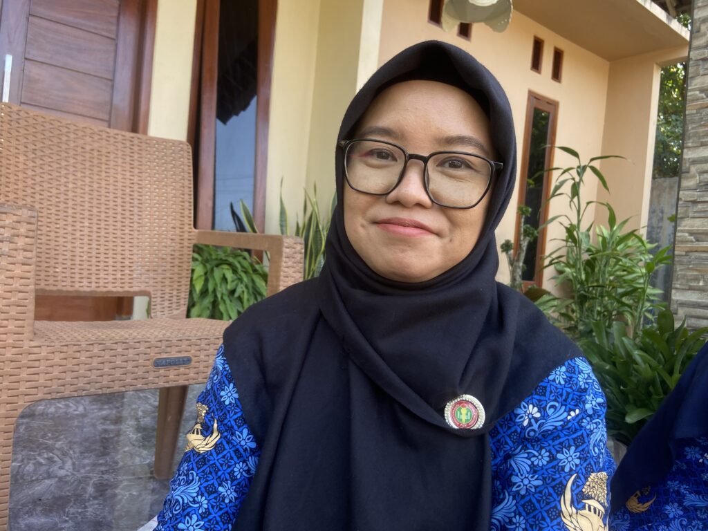IMG_7487 - Mabur.co Portrait of a person wearing a black hijab and glasses outdoors beside a beige building and wicker chairs.