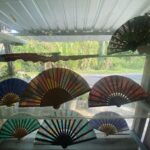 Colorful fold-out paper fans arranged along a windowsill with greenery outside.