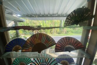 Colorful fold-out paper fans arranged along a windowsill with greenery outside.