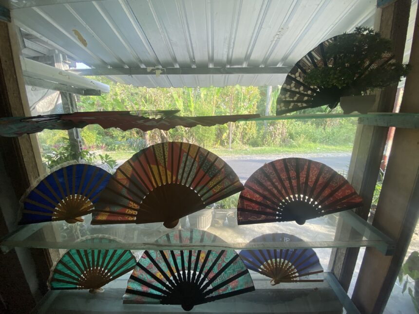 Colorful fold-out paper fans arranged along a windowsill with greenery outside.