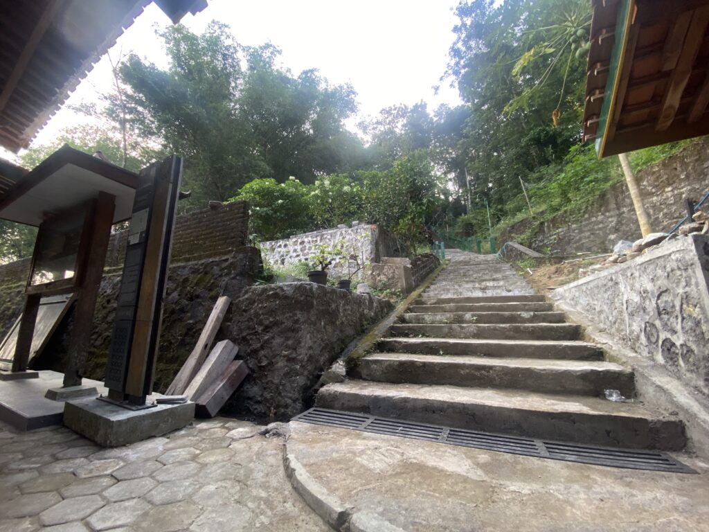 IMG_7781 - Mabur.co Stone stairway winding uphill with stone walls and lush trees on both sides, in a rustic outdoor setting.