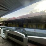 Covered outdoor walkway beside a red-tiled roof building with yellow and black railing, under a metal canopy.