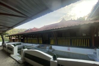 Covered outdoor walkway beside a red-tiled roof building with yellow and black railing, under a metal canopy.