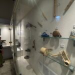 Museum display case with numbered wooden artifacts mounted on the wall; glass barrier reflects visitors in the foreground.