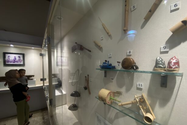 Museum display case with numbered wooden artifacts mounted on the wall; glass barrier reflects visitors in the foreground.