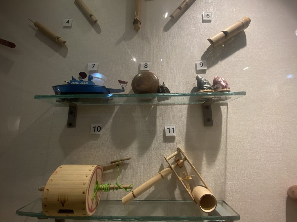 Display shelf of wooden crafts labeled with numbers 4–11, including a blue model boat on the left, a carved wooden bowl in the center, and other wooden objects.