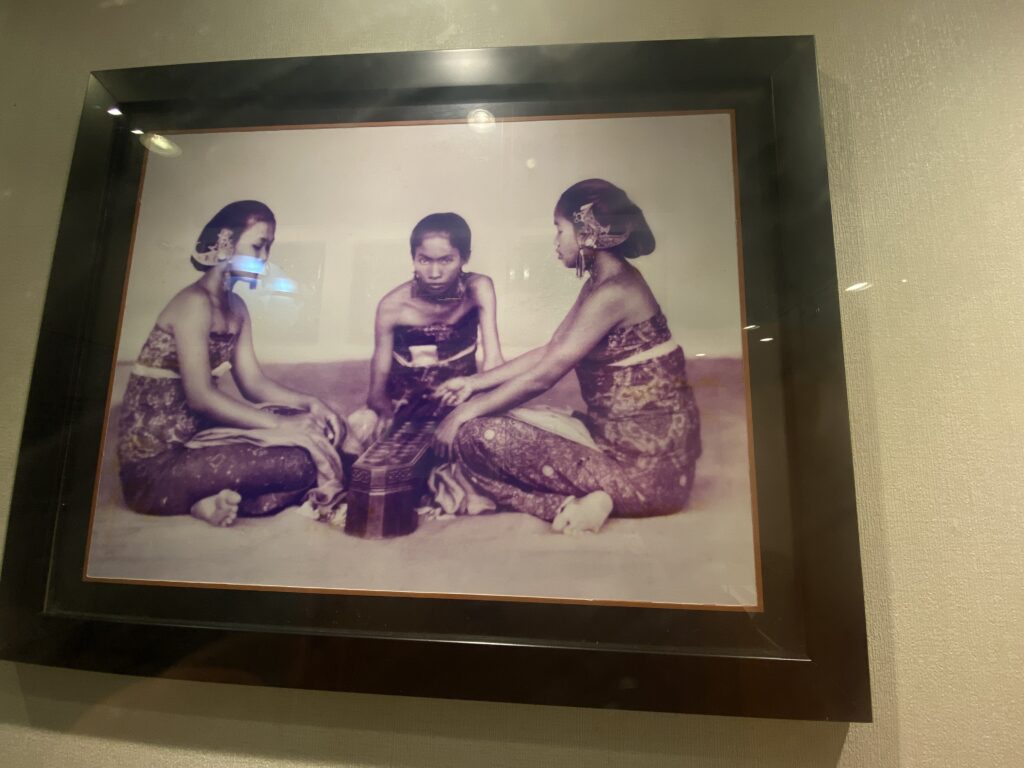 Vintage photo of three people in traditional dress posing together, two women with ornate headpieces flanking a man in center.