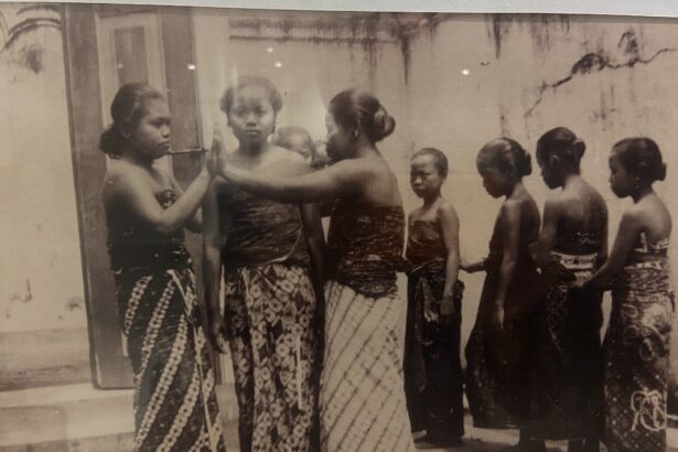 Vintage black-and-white photo of young women in patterned saris standing in a line outdoors; one resting a hand on another's shoulder.