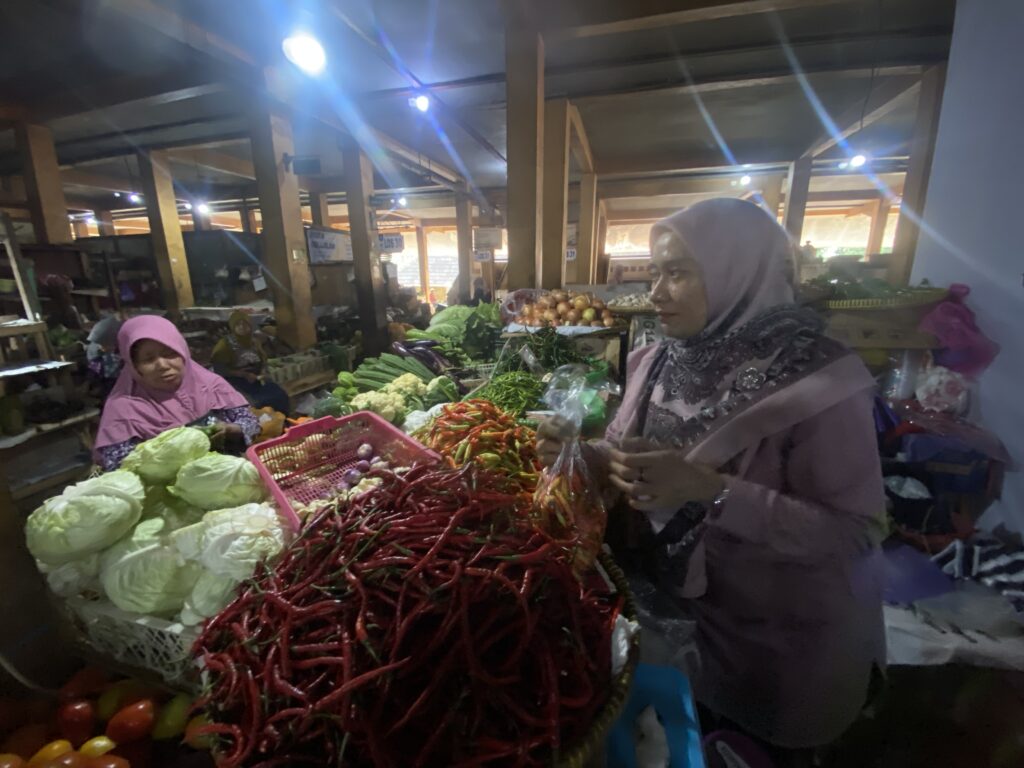 IMG_8148 - Mabur.co Women in hijabs stand at a bustling market stall with peppers, cabbage and other vegetables on display.
