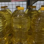 Rows of clear plastic bottles filled with yellow cooking oil on a store shelf with yellow caps