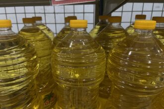 Rows of clear plastic bottles filled with yellow cooking oil on a store shelf with yellow caps