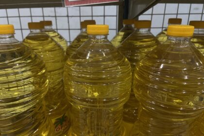 Rows of clear plastic bottles filled with yellow cooking oil on a store shelf with yellow caps